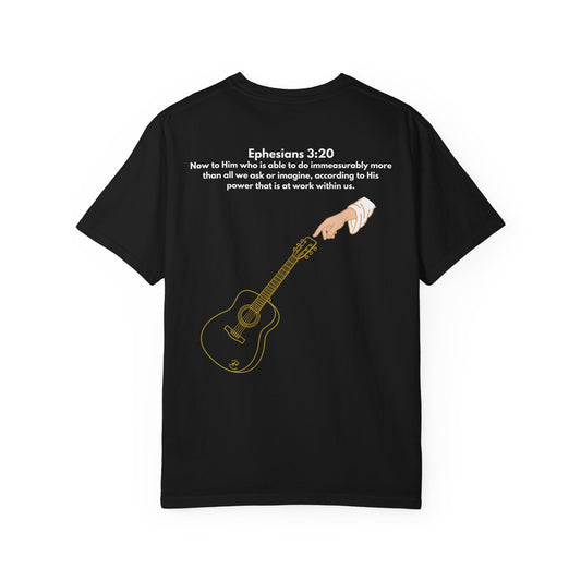 back Premium garment-dyed black Christian worship t-shirt with gold acoustic guitar and guiding hand back design, Ephesians 3:20 Bible verse.